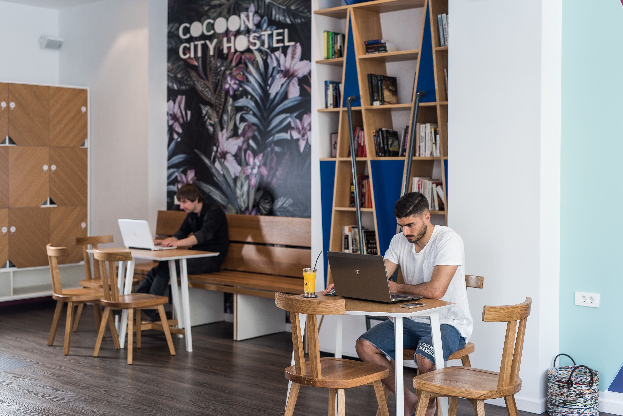 Een modern hostelinterieur met houten meubels, een boekenkast en een poster die het hostel promoot.