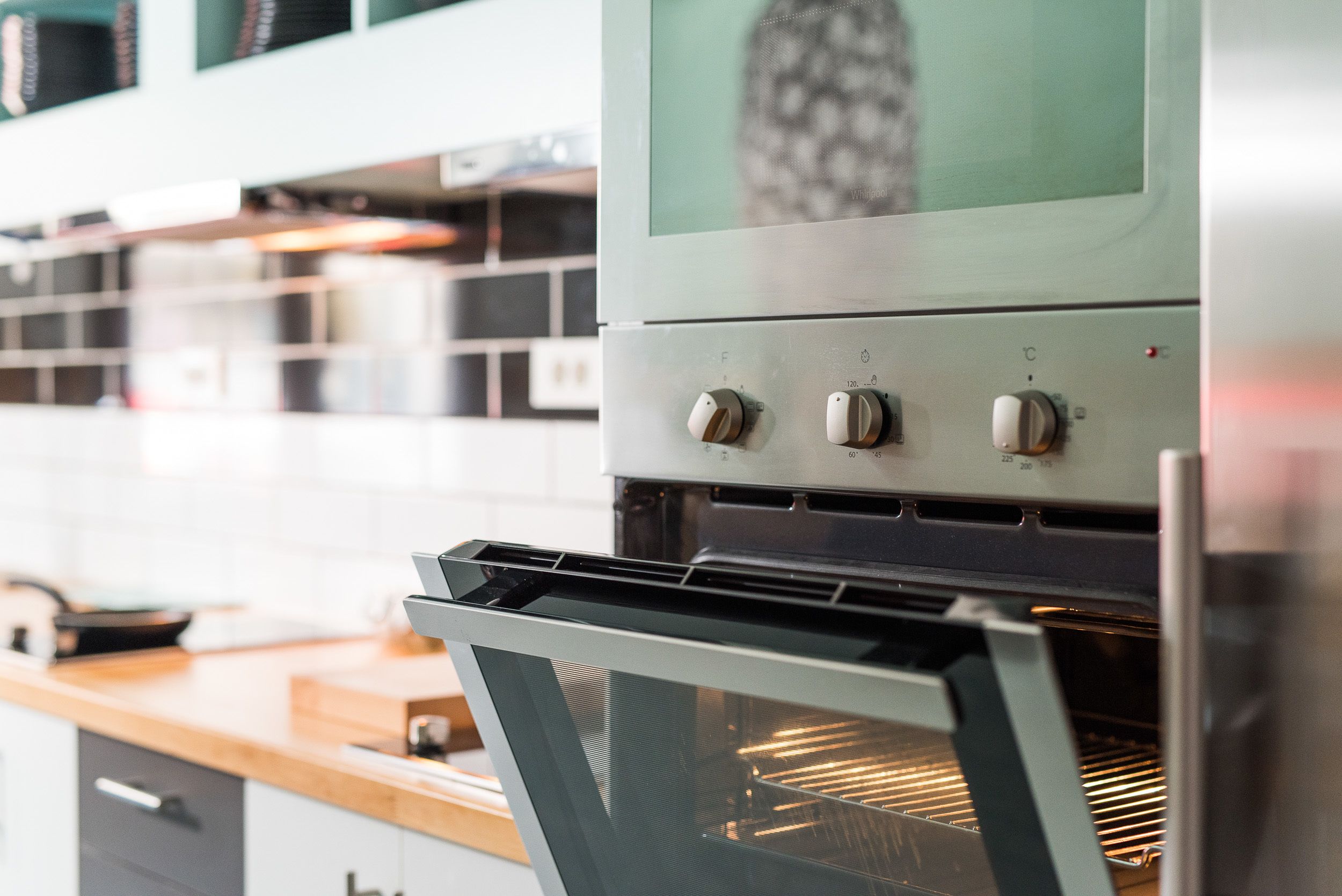 An oven with control knobs and a glass door, part of a kitchen with white cabinets and a wooden countertop.