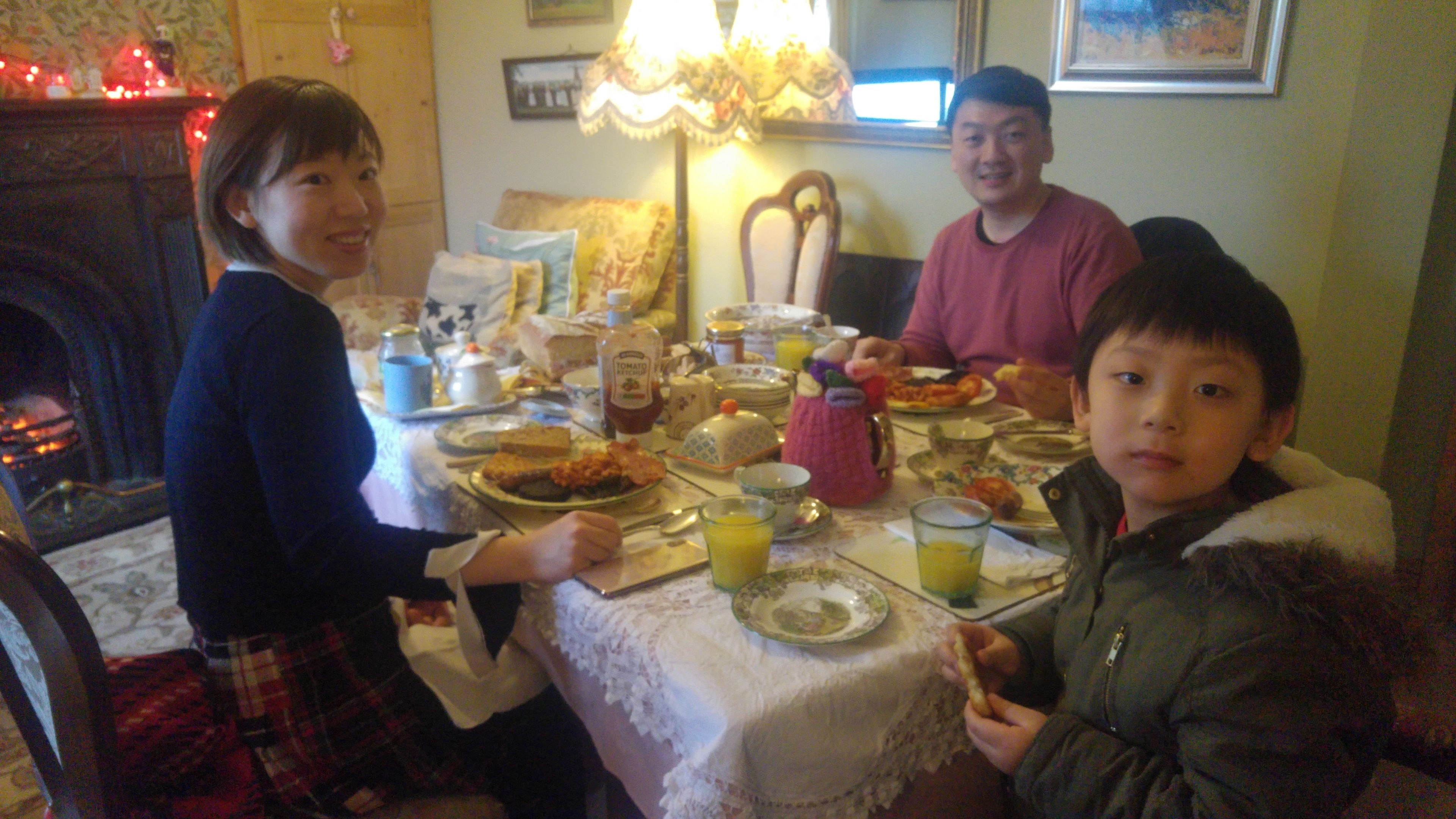 Una mesa de comedor servida con diversos platos y bebidas, rodeada de gente.