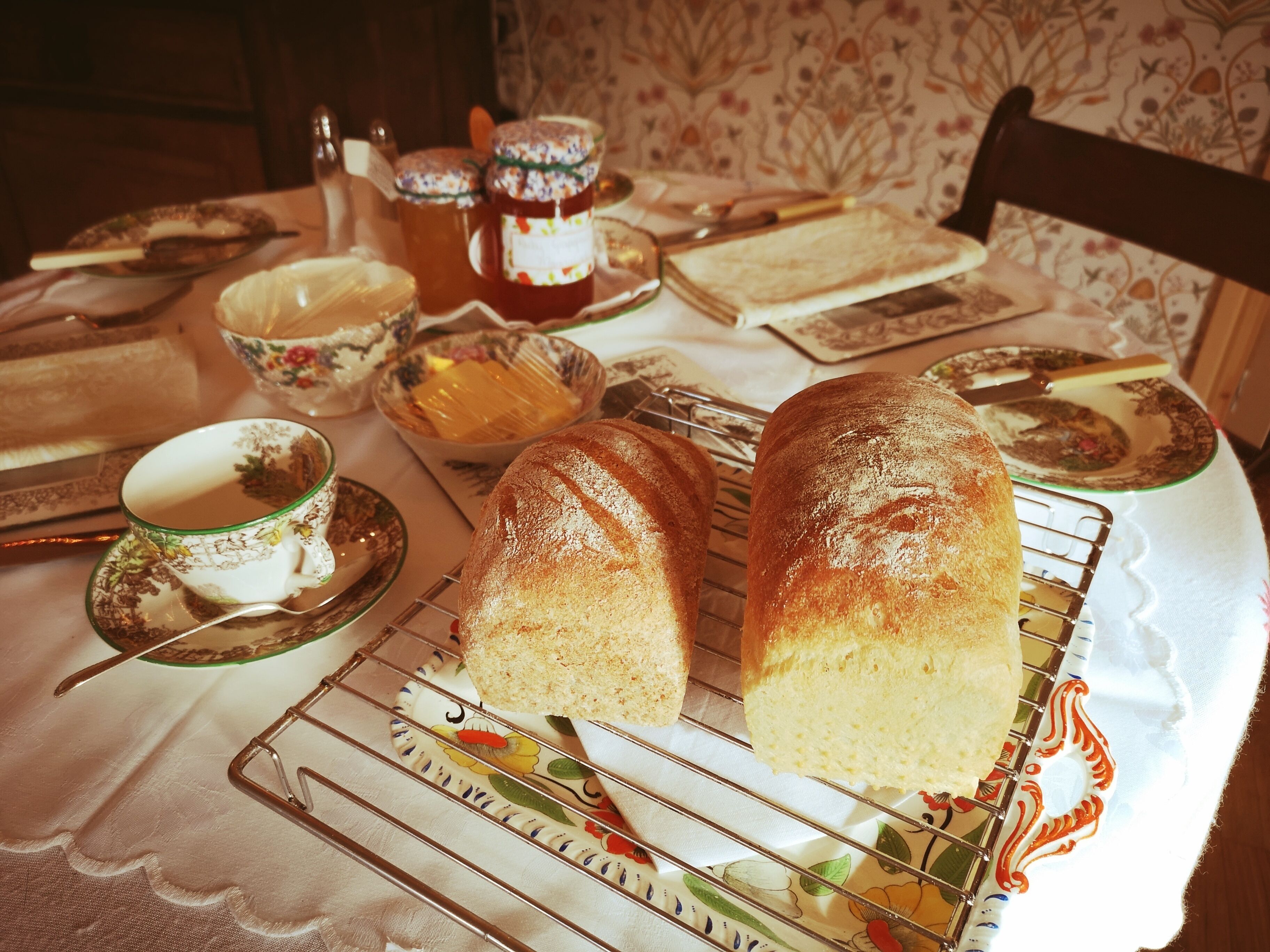 Una mesa con pan, una tetera, tazas y un plato con motivos florales.