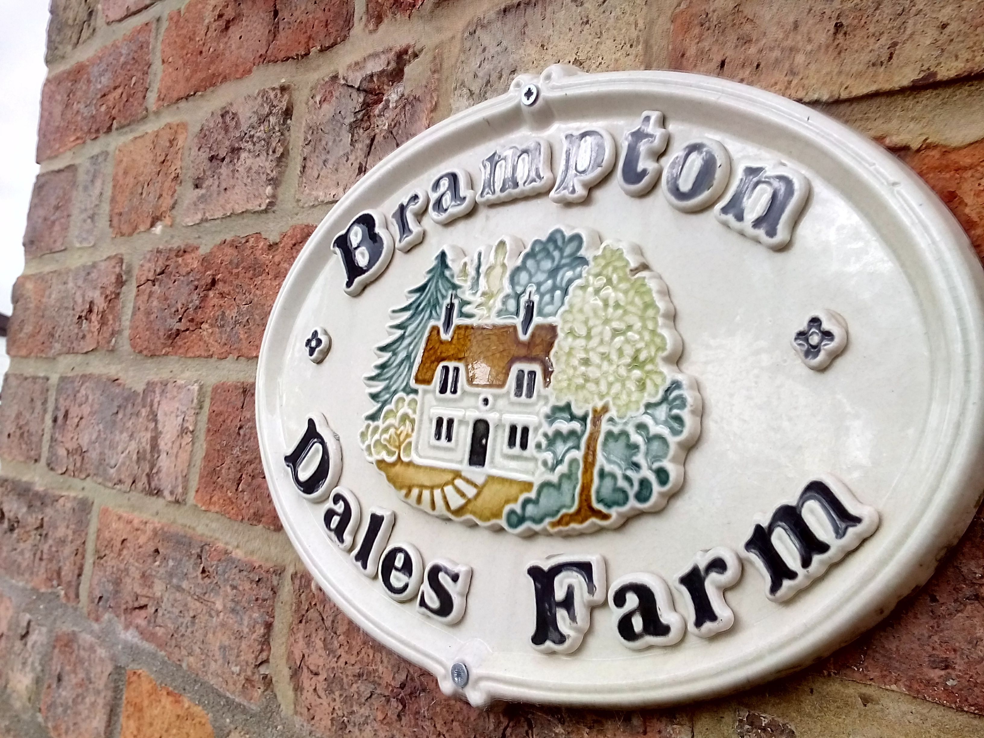 Ein Schild mit dem Schriftzug „Brampton Dales Farm“ und einem dekorativen Haus-Wappen, umgeben von Bäumen.