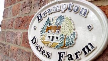 Ein Schild mit dem Schriftzug „Brampton Dales Farm“ und einem dekorativen Haus-Wappen, umgeben von Bäumen.