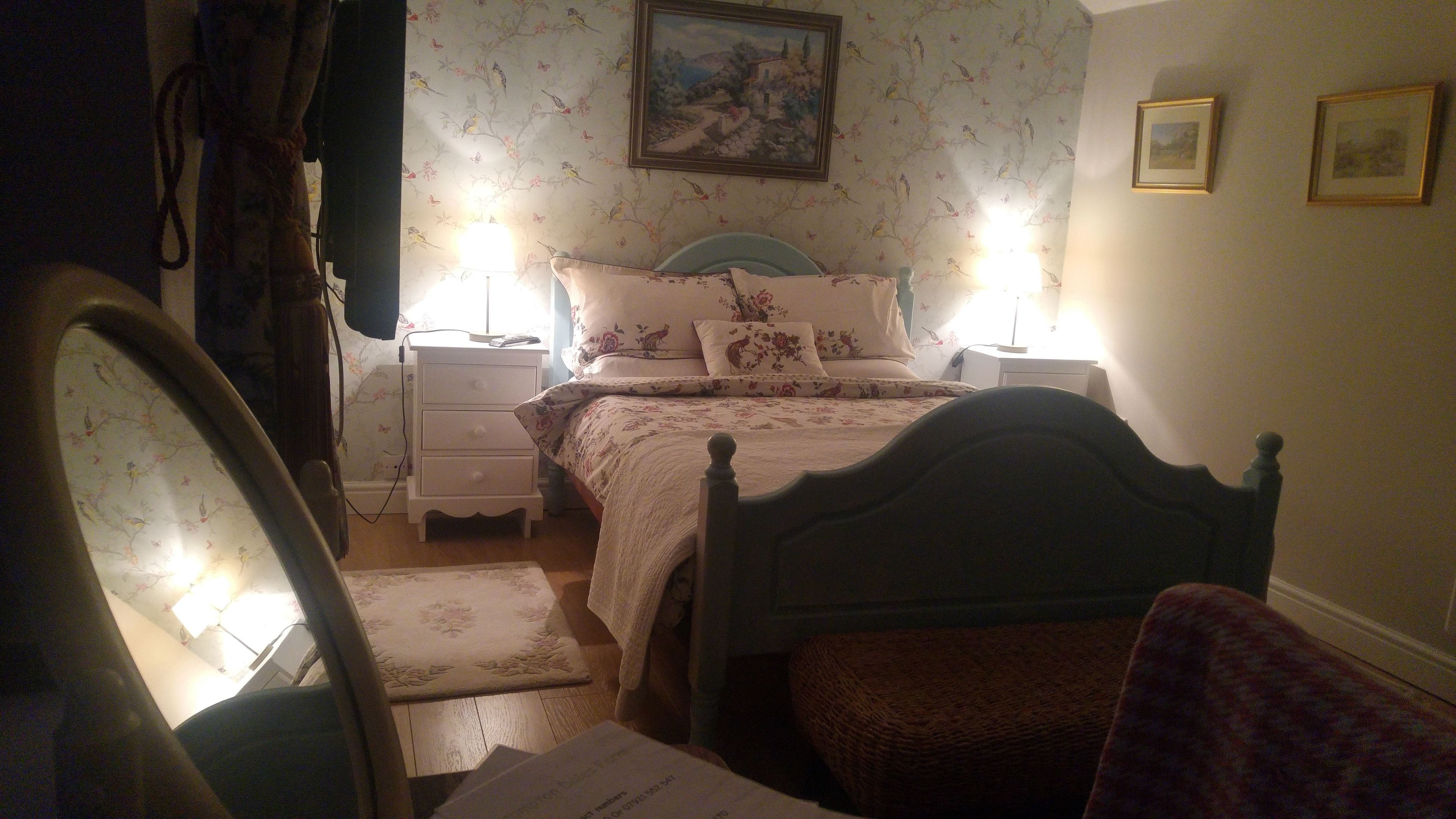 Un dormitorio con cama, mesitas de noche, una silla y una lámpara.