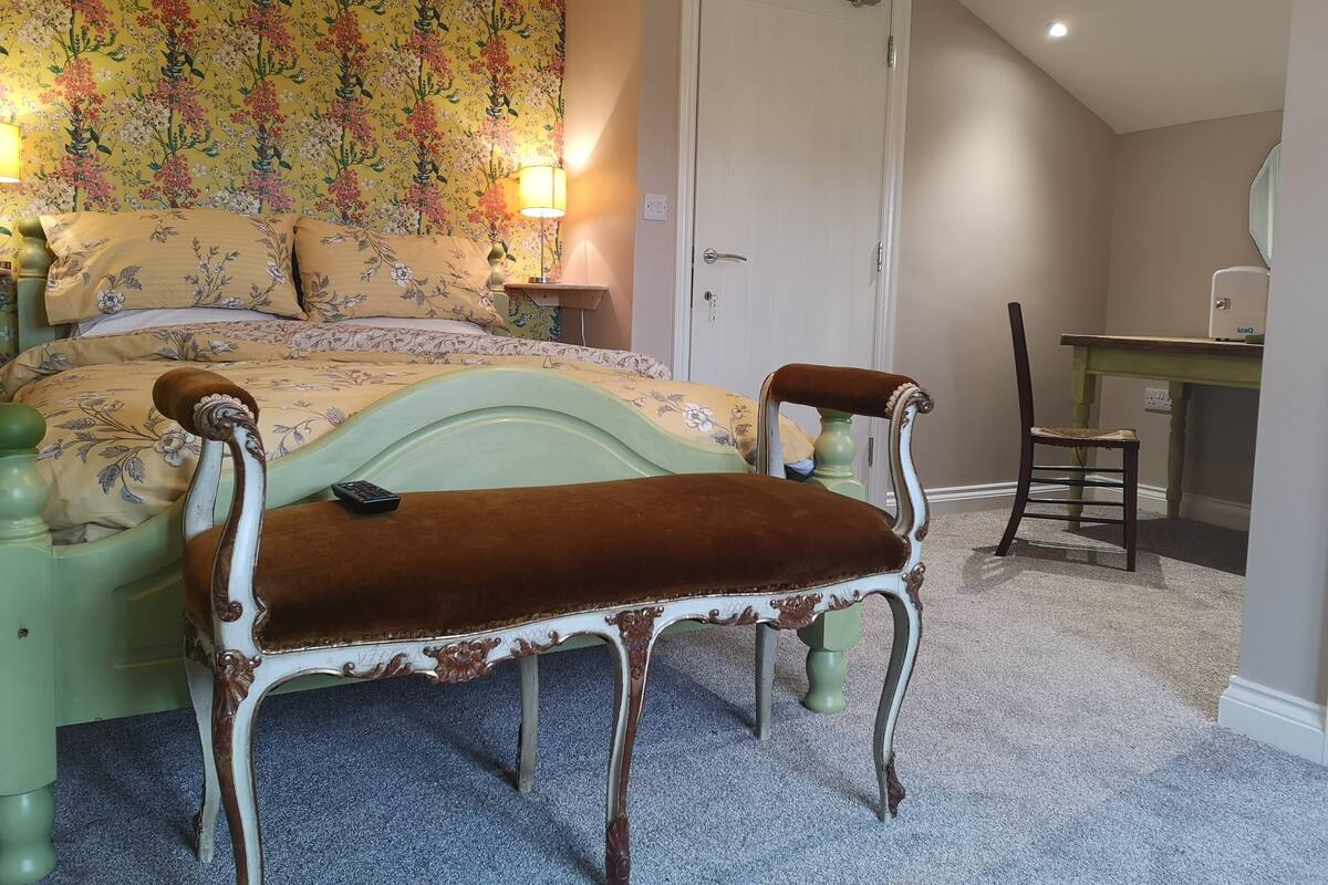 Quarto com cama, cadeira, escrivaninha e papel de parede floral.