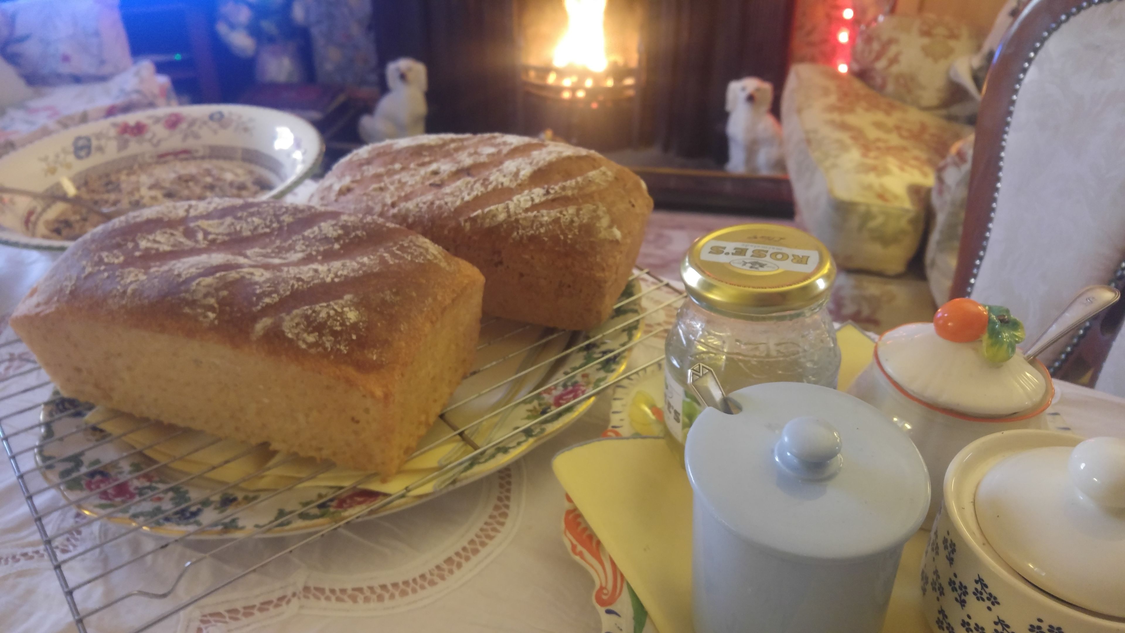 A table with two loaves of bread, a jar of honey, and a teapot.