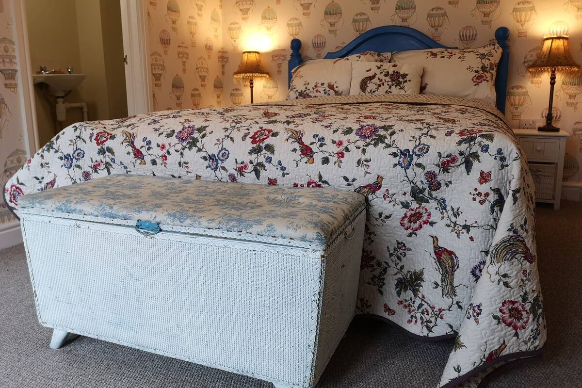 Um quarto com uma cama, mesa de cabeceira, abajur e uma pequena mesa.