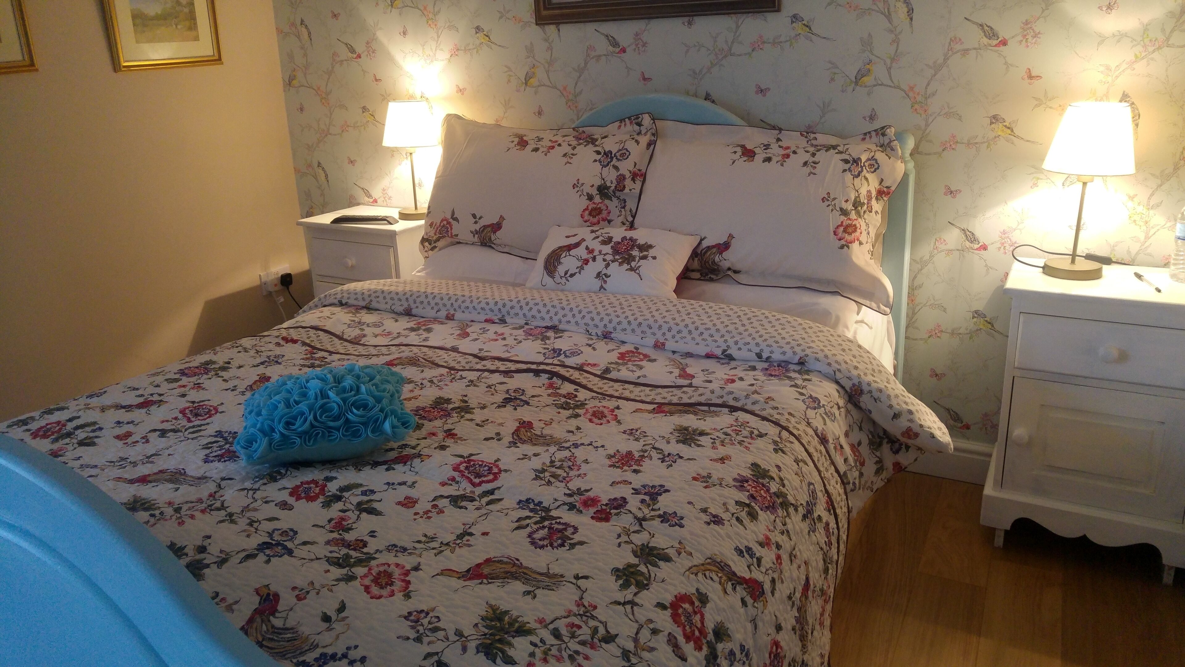 A neatly made bed with floral bedding, two bedside lamps, and a nightstand with a lamp.