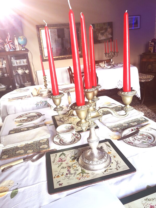 Una mesa de comedor preparada con velas rojas, cubiertos y un mantel floral.