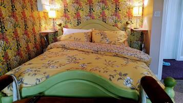 A bed with floral bedding and a green headboard, two bedside lamps, and a remote control on the bed.