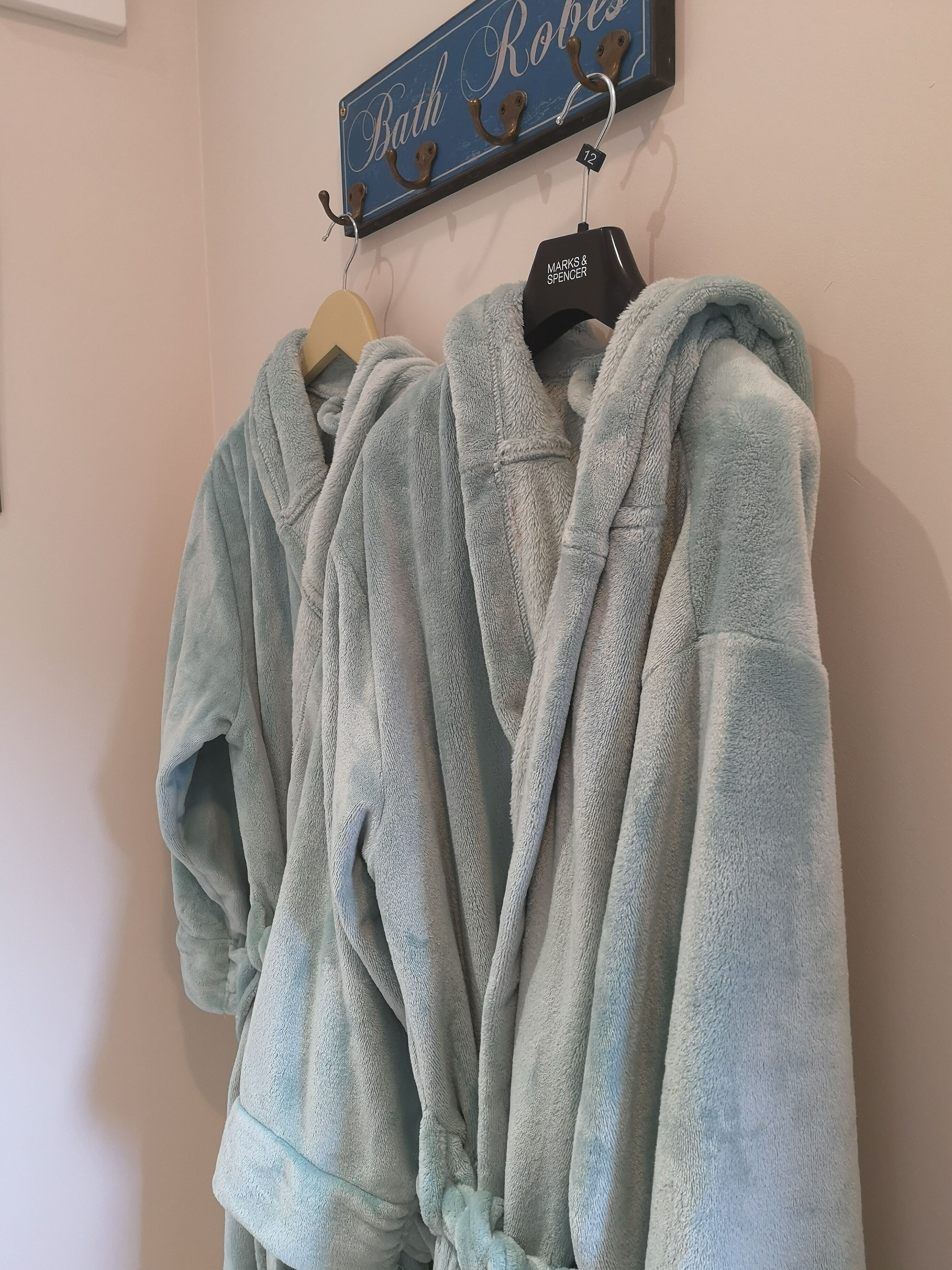 Deux peignoirs bleu clair sont suspendus à un porte-manteau, au-dessus desquels on peut lire l’inscription : « Peignoirs de bain ».