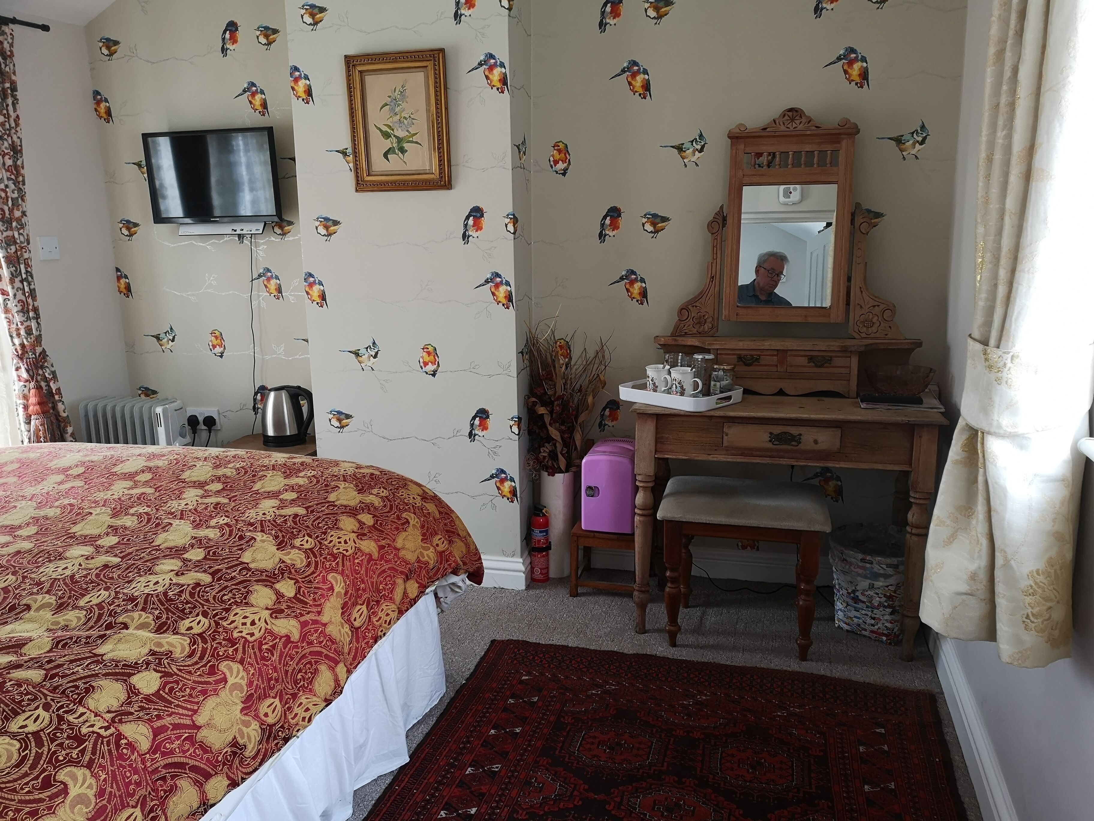A bedroom with a bed, a dresser, a mirror, a TV, and a radiator.