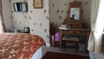Un dormitorio con una cama, un aparador, un espejo, un televisor y un radiador.