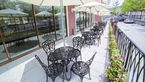 An outdoor patio with tables and chairs, large umbrellas, and a view of the street.