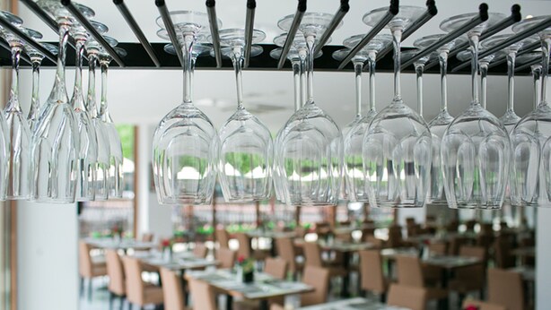 A restaurant with multiple tables and chairs, and wine glasses hanging from the ceiling.