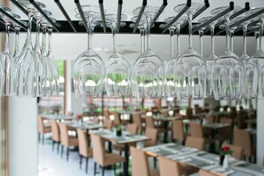 Een restaurant met meerdere tafels en stoelen, en wijnglazen aan het plafond.