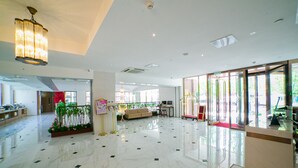 A spacious lobby with a marble floor, a reception desk, a seating area, and large windows allowing natural light.