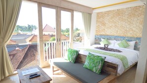 A bedroom with a bed, a bench, a table, and a view of the outside. - Green Studio Apartment Sanur (Denpasar)