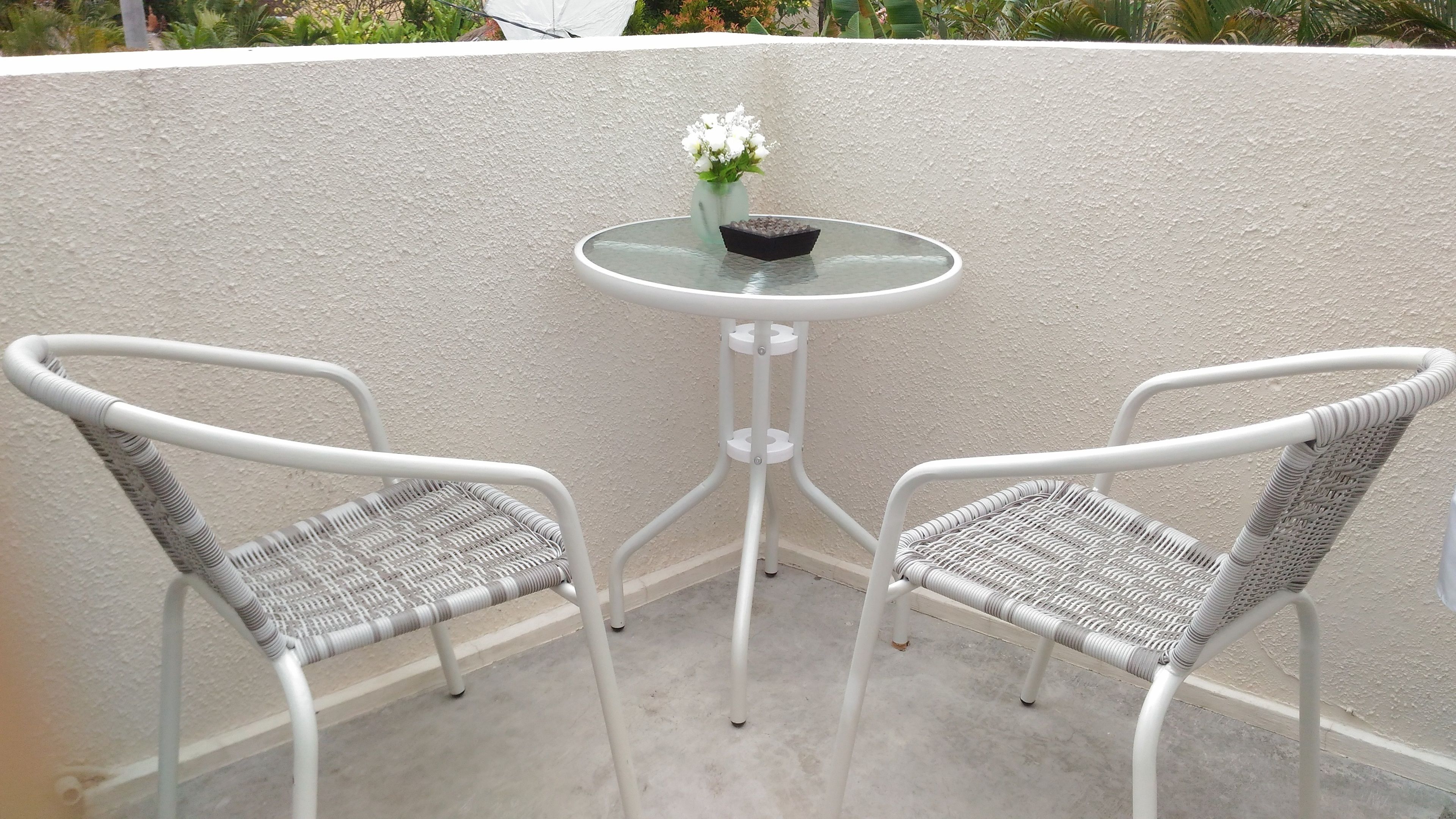 Two white wicker chairs with a glass table and a vase of white flowers on a balcony.