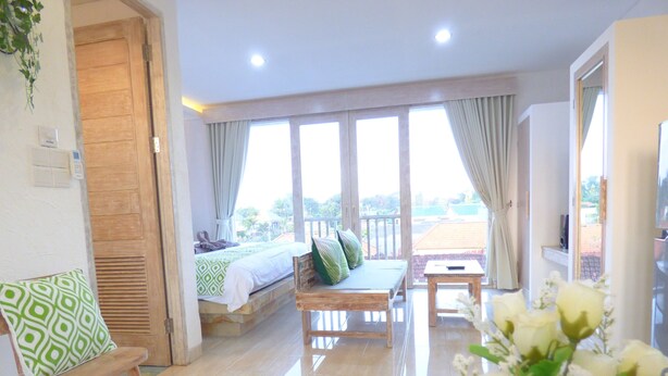 A room with a bed, a wooden bench, a small table, and a balcony with a view. - Green Studio Apartment Sanur (Denpasar)