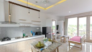 A modern kitchen with a dining area, a TV, and a balcony with a view. - Green Studio Apartment Sanur (Denpasar)