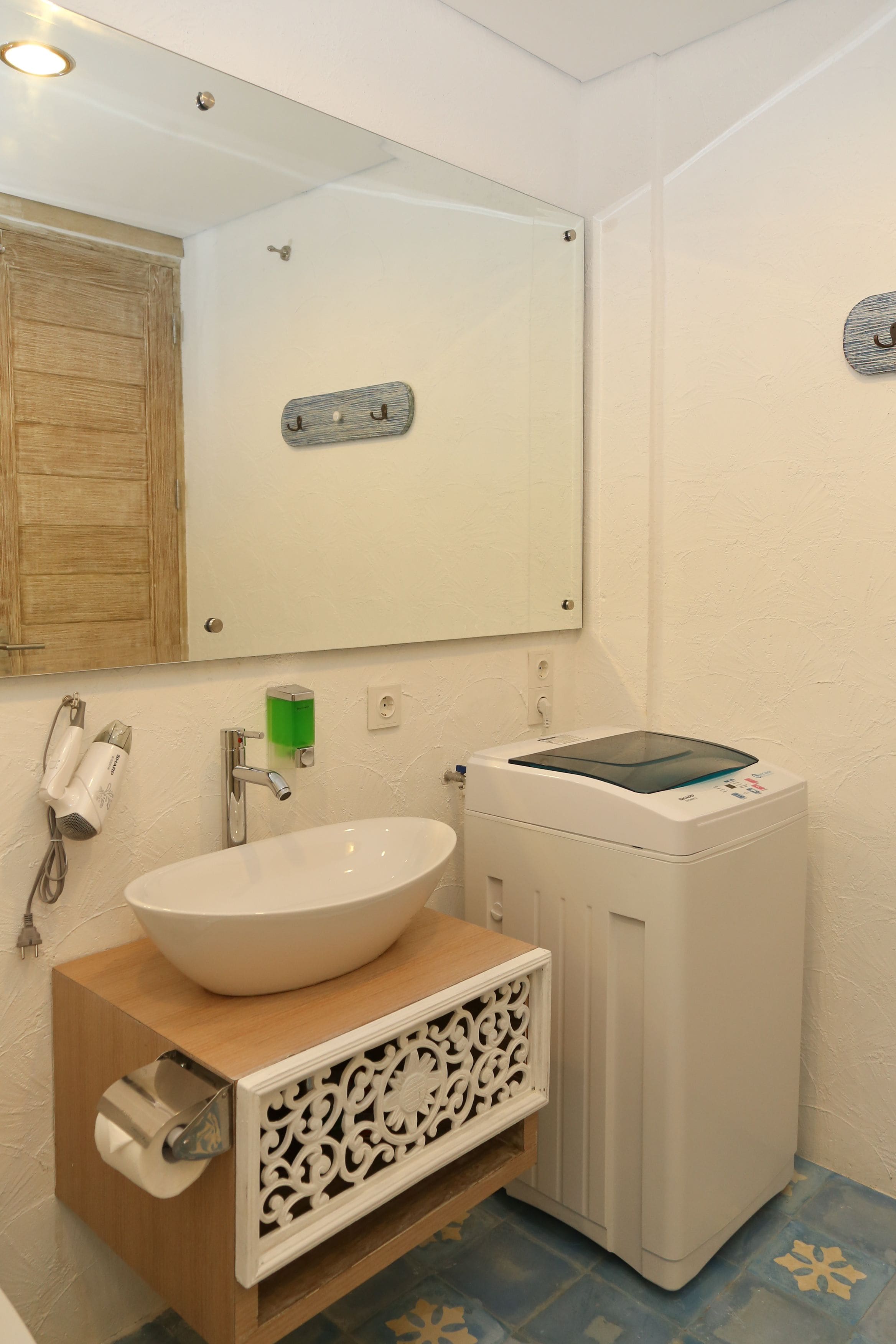 A bathroom with a white sink, a mirror, a wooden cabinet, a hairdryer, and a washing machine.