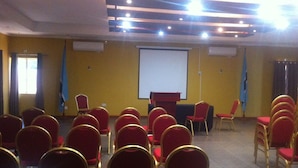 A conference room with rows of red chairs, a podium, and a projection screen. - Exec Closets Hotel (Gaborone)