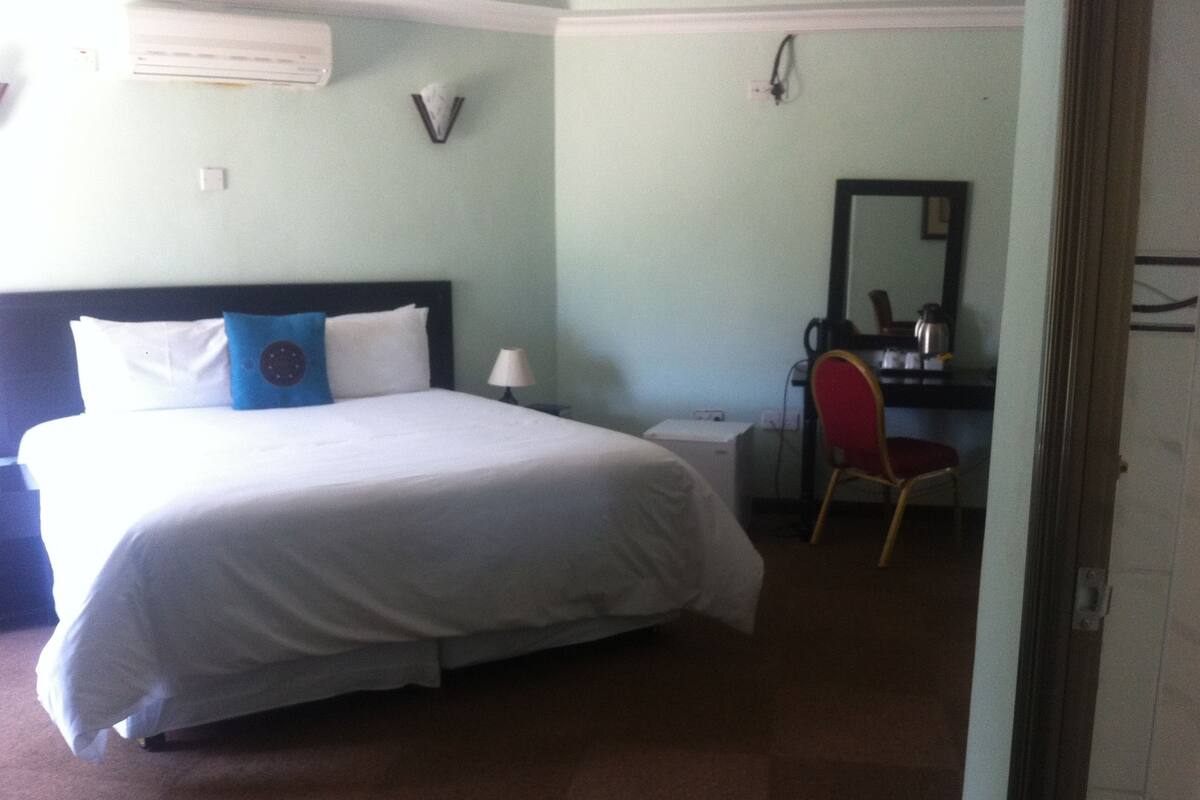 A hotel room with a bed, a desk, a chair, and a mirror.