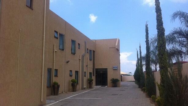 A building with a reception area, a paved walkway, and tall cypress trees. - Exec Closets Hotel (Gaborone)