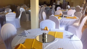 A banquet hall with round tables set for dining, white tablecloths, and yellow napkins. - Exec Closets Hotel (Gaborone)