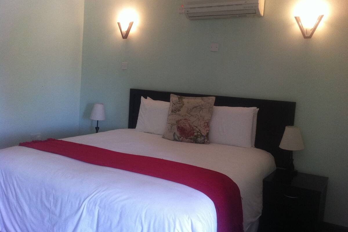 A neatly made bed with a red blanket, two wall-mounted lamps, and an air conditioning unit above the bed.