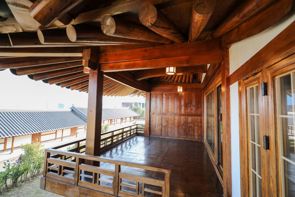 A wooden interior with a balcony, traditional wooden doors, and a view of the outside.