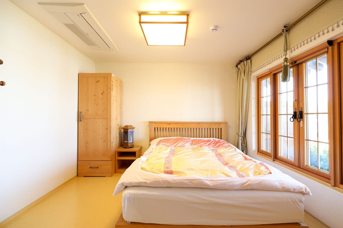 A bedroom with a bed, a wooden wardrobe, a nightstand, and a window with curtains.