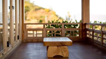A wooden bench with a polished tabletop in a covered outdoor area with wooden railings and a view of a hillside.