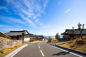 A traditional Japanese building with a curved road leading to it, surrounded by dry grass and a stone wall. - Hanok Hotel Odongjae (Yeosu)