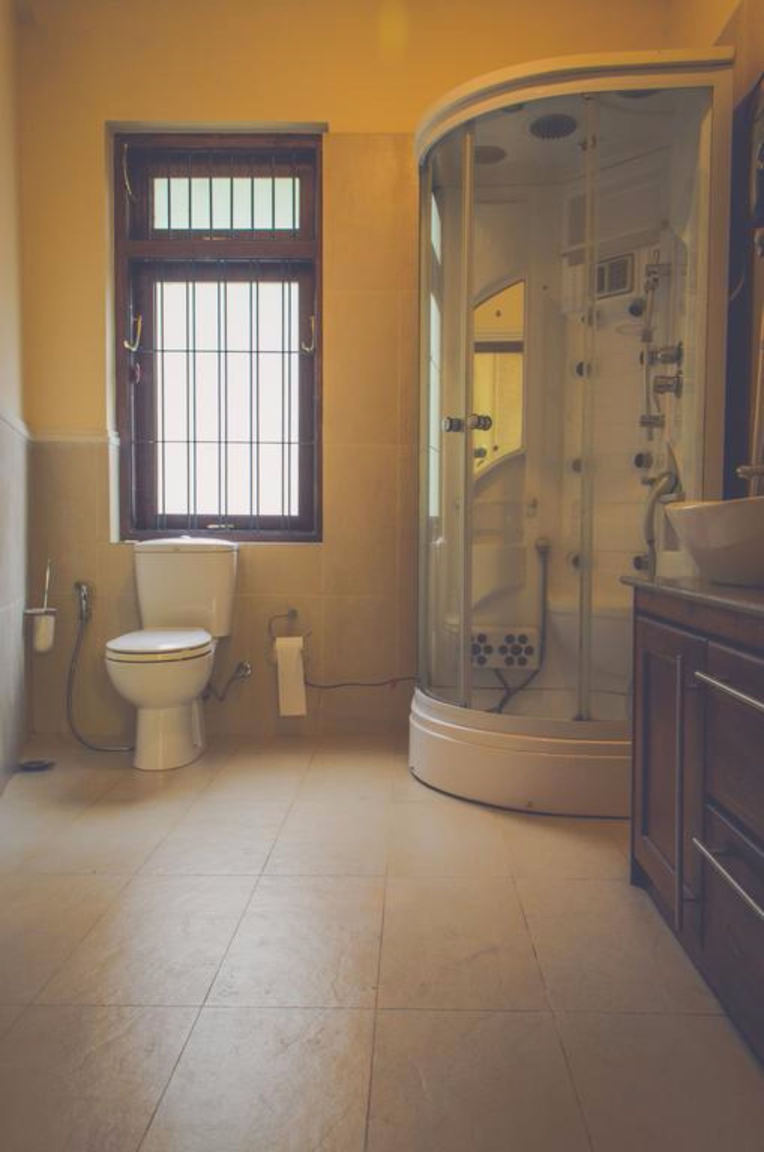 A bathroom with a toilet, a window, a shower enclosure, and a sink.