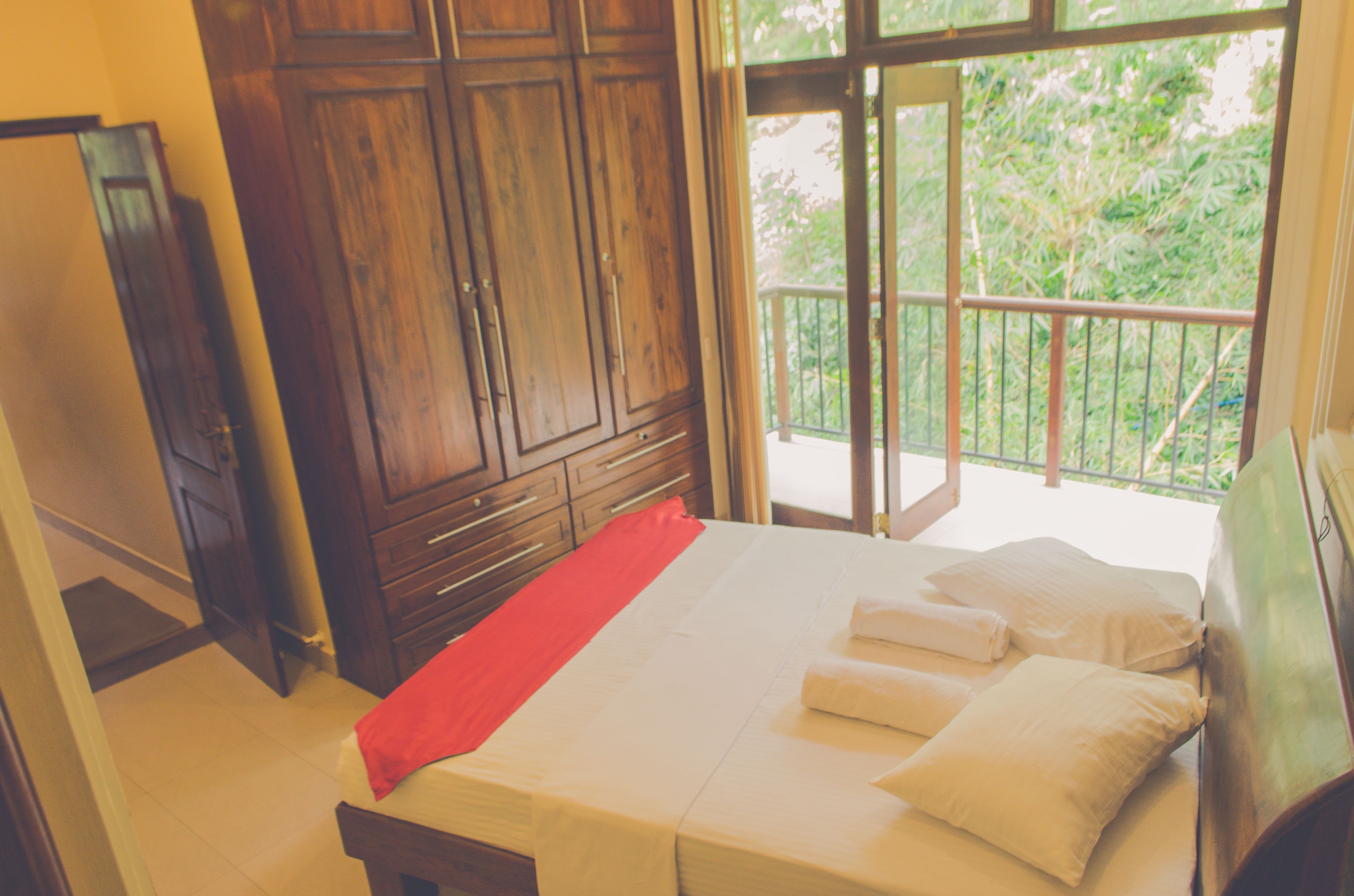 Un dormitorio con cama, armario de madera y balcón con vistas a la vegetación.