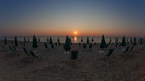 A beach with rows of green umbrellas and lounge chairs facing the sunset. - Hotel Ambasciatori (Pineto)