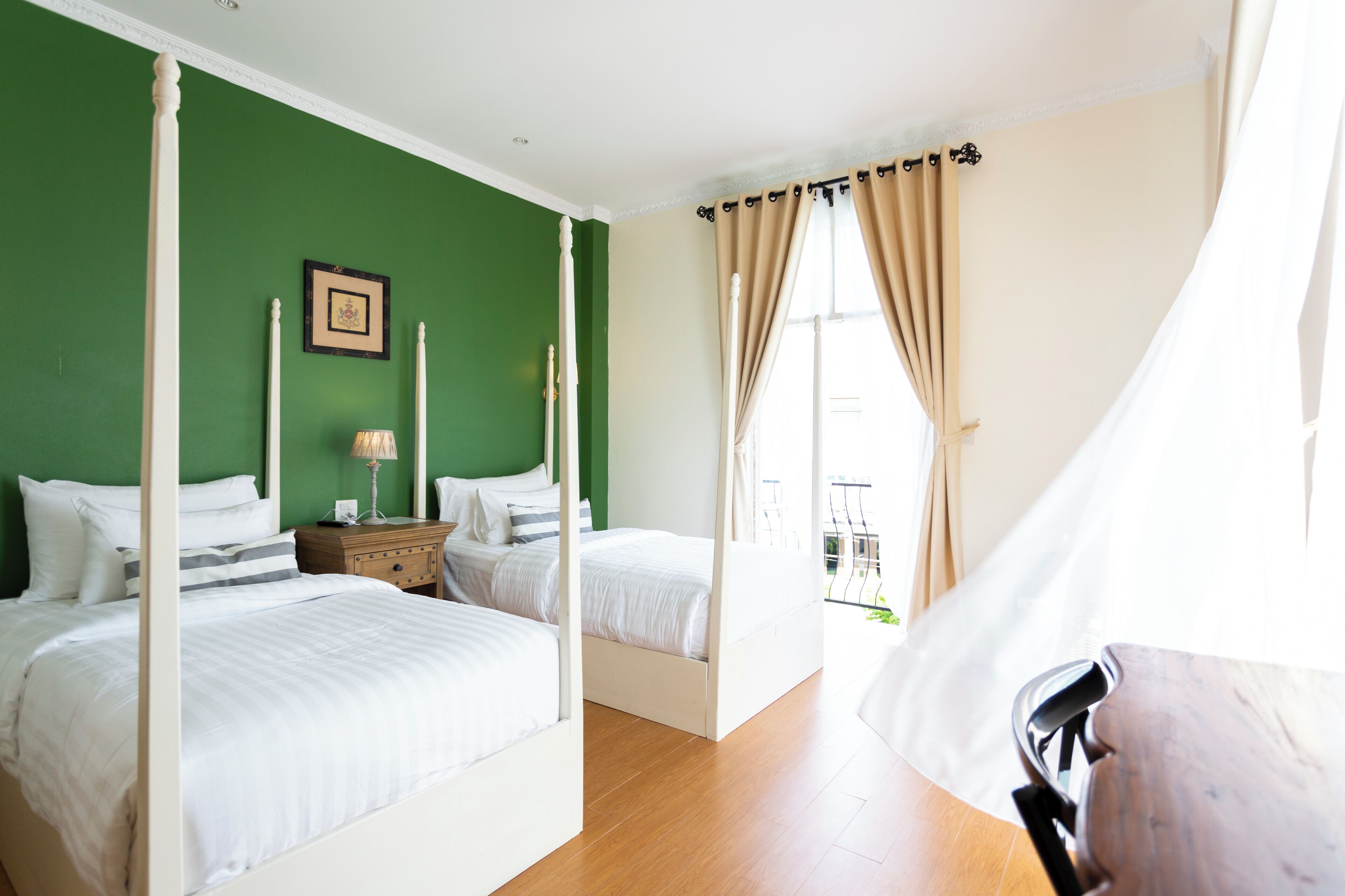 A four-poster bed with white bedding, a nightstand with a lamp, and a green wall.