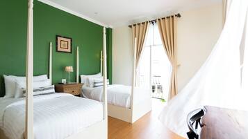 A four-poster bed with white bedding, a nightstand with a lamp, and a green wall.