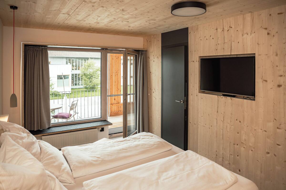 Une chambre avec deux lits, un téléviseur fixé au mur et une porte-fenêtre coulissante donnant sur un balcon extérieur.