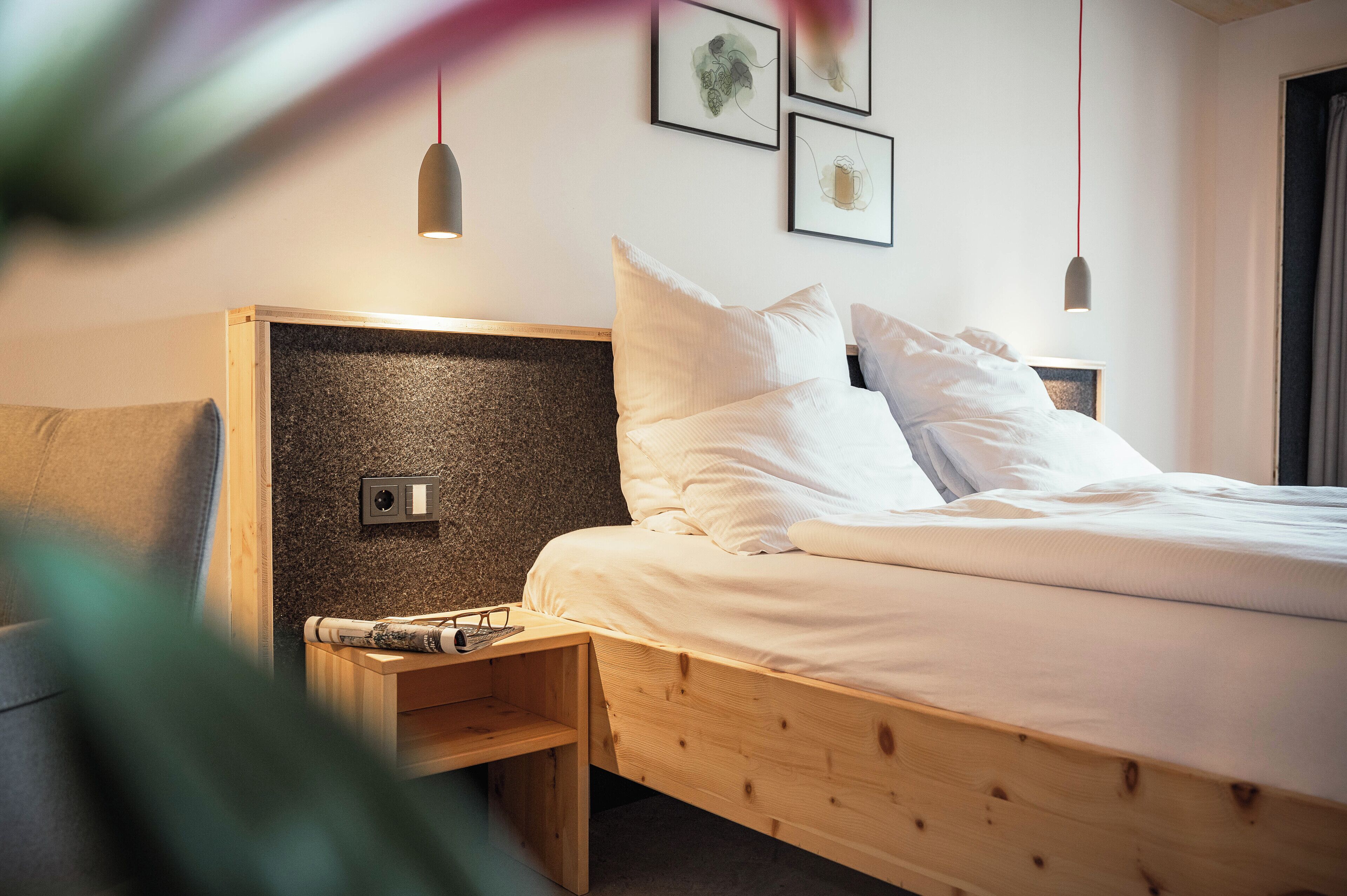 A neatly made bed with white linens, a wooden headboard, and a bedside table with glasses and a book.
