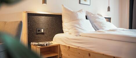 A neatly made bed with white linens, a wooden headboard, and a bedside table with glasses and a book.