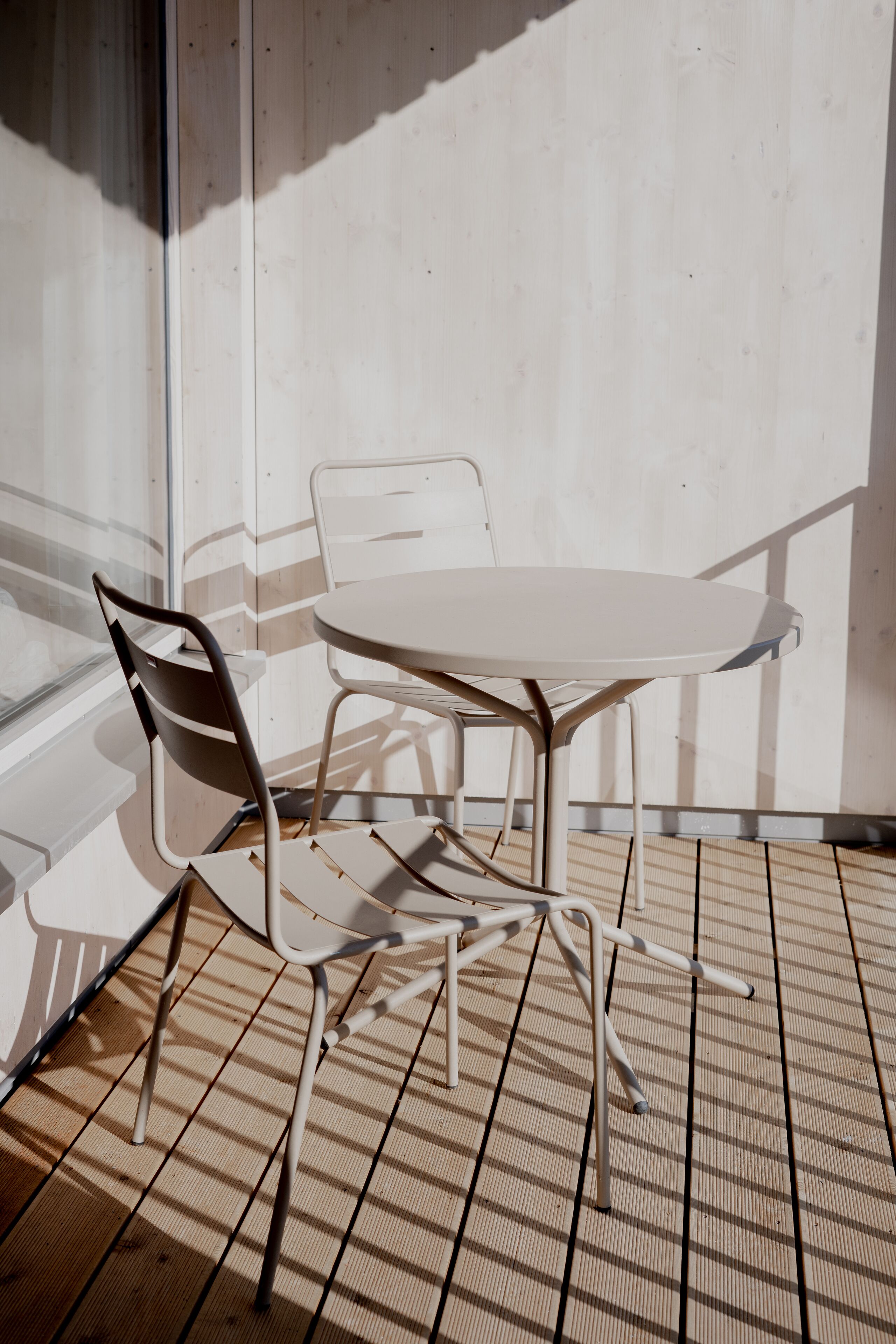 A table and chairs on a wooden deck with a view of a building in the background.