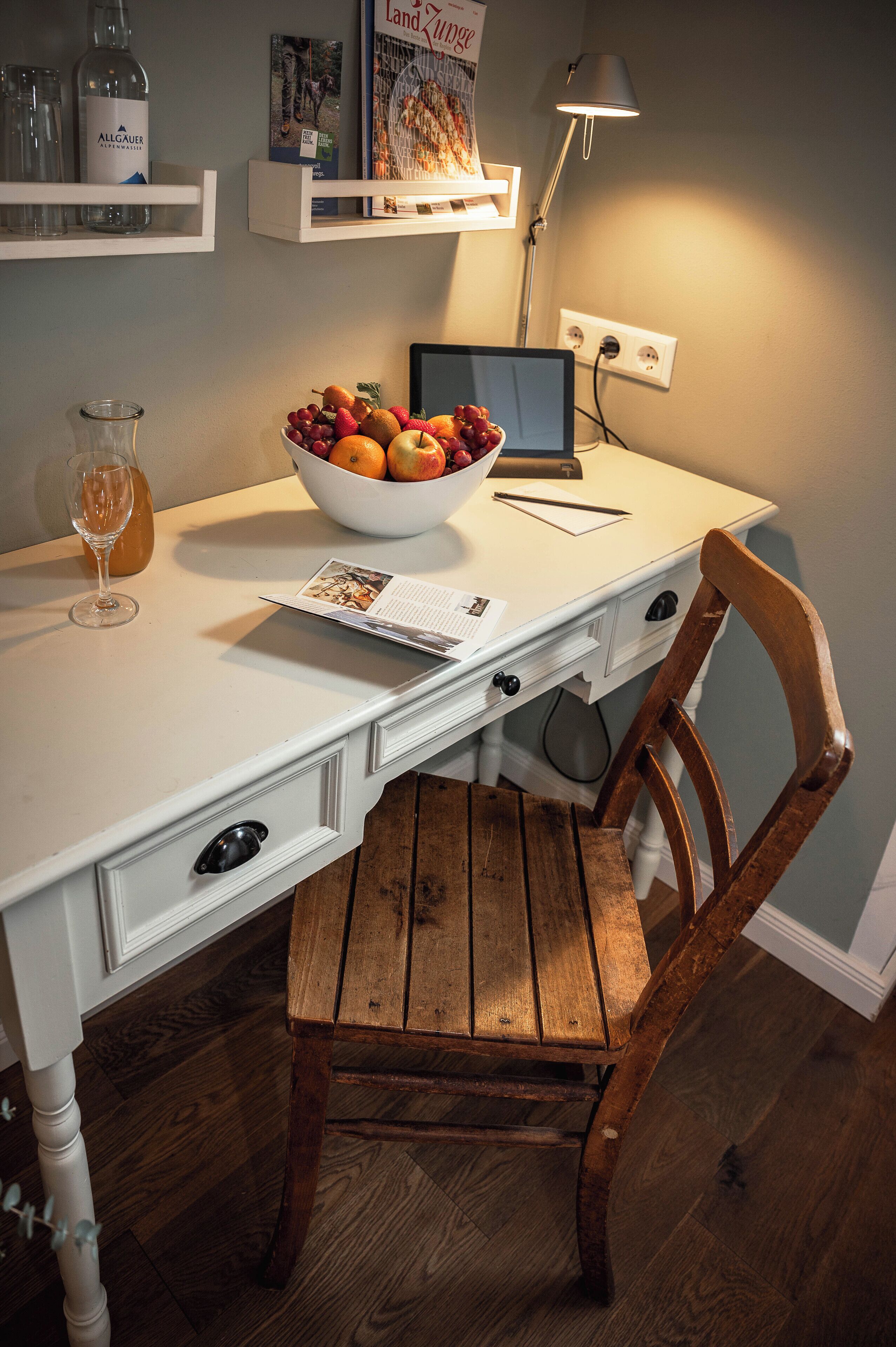 A white desk with a laptop, a bowl of fruit, a glass of juice, and a notebook.