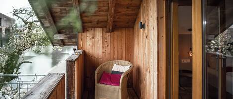 Un balcón de madera con una silla de mimbre y una puerta de cristal que da a una habitación interior.