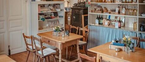 Un rincón comedor acogedor con mesas y sillas de madera, rodeado de estantes llenos de alimentos y botellas.