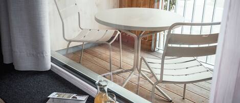 A balcony with a round table and two white chairs, a glass pitcher, and a glass of drink on the floor.
