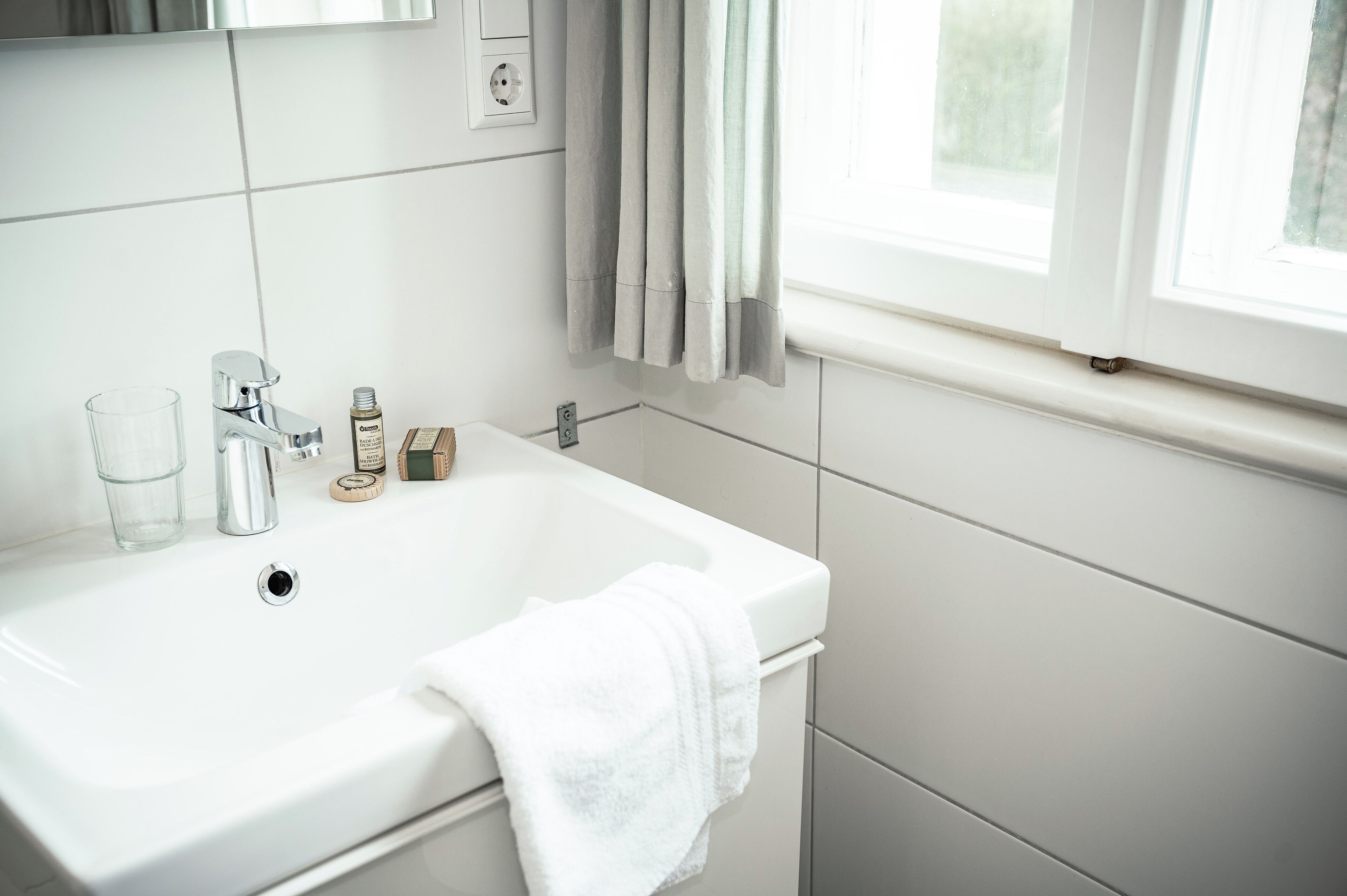 Een witte badkamer met een wastafel, kraan en een handdoek aan de zijkant.