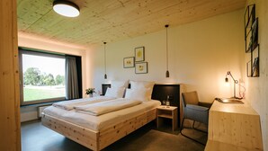 A wooden-framed bedroom with a large bed, a desk, and a chair. There are framed pictures on the wall and a window with curtains.