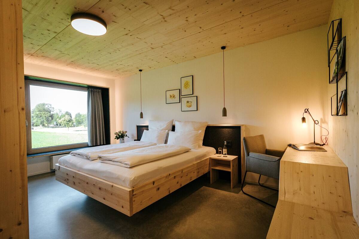 Une chambre à coucher avec un cadre en bois, comprenant un grand lit, un bureau et une chaise. Les murs sont ornés de tableaux encadrés et il y a une fenêtre avec des rideaux.